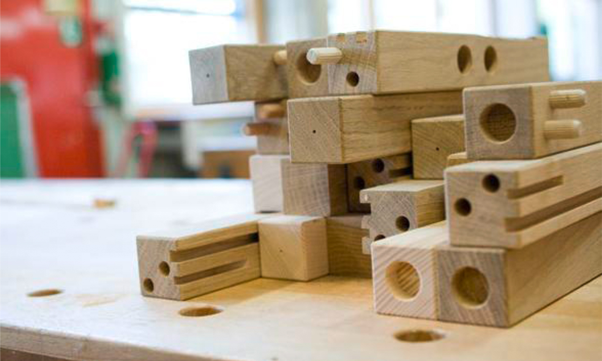 Meherere Einzelteile aus Holz liegen aufeinandergestapelt auf einer Werkbank.